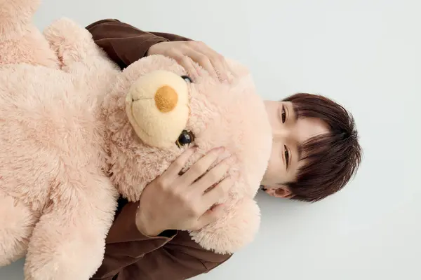 A young handsome man cuddles a fluffy teddy bear while lying down, radiating warmth and joy. — Stock Photo