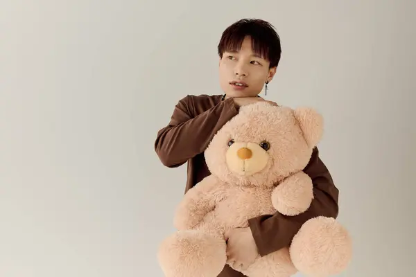 Un charmant jeune homme asiatique embrasse un ours en peluche dans un studio inspiré par la lumière, respirant la chaleur. — Photo de stock