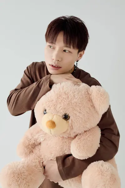 Un jeune homme tient un ours en peluche, respirant chaleur et charme dans un cadre calme. — Photo de stock