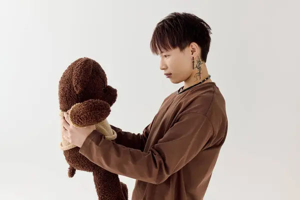 A young handsome asian man gazes affectionately at a soft plush bear in a minimalist room. — Stock Photo