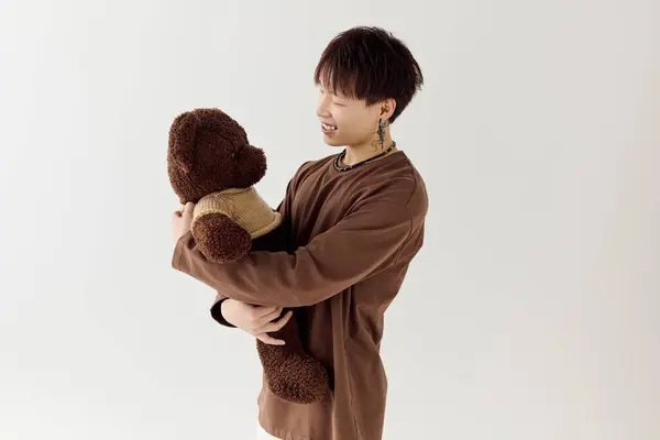 A handsome young asian man smiles while embracing a large teddy bear in a modern studio setting. — Stock Photo