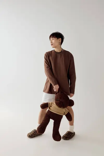 Young handsome man stands confidently, gripping a teddy bear in a bright, spacious studio. — Stock Photo