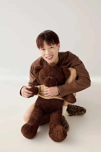 Un jeune homme asiatique sourit joyeusement, embrassant un ours en peluche doux dans un moment ludique. — Photo de stock