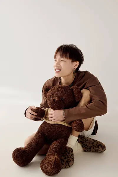 A joyful young Asian man holds a large teddy bear in a warm, minimalistic setting. — Stock Photo