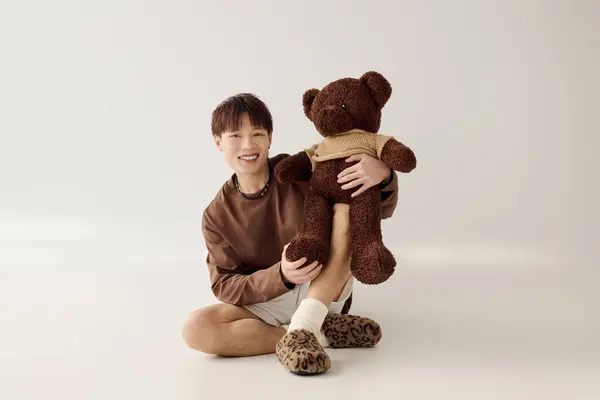 A young man sits on the floor, joyfully hugging a teddy bear, radiating warmth. — Stock Photo