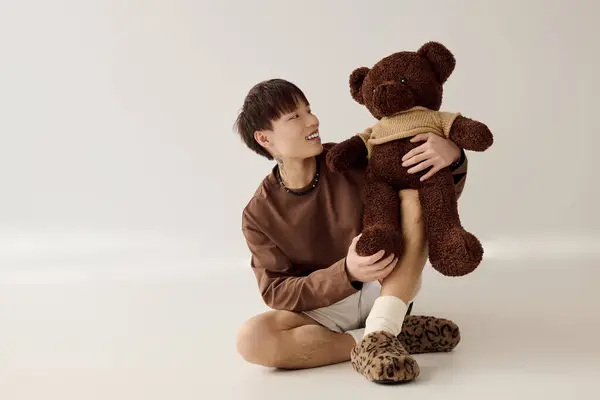 Joyeux jeune homme s'engage dans une interaction ludique avec un ours en peluche mignon assis confortablement. — Photo de stock