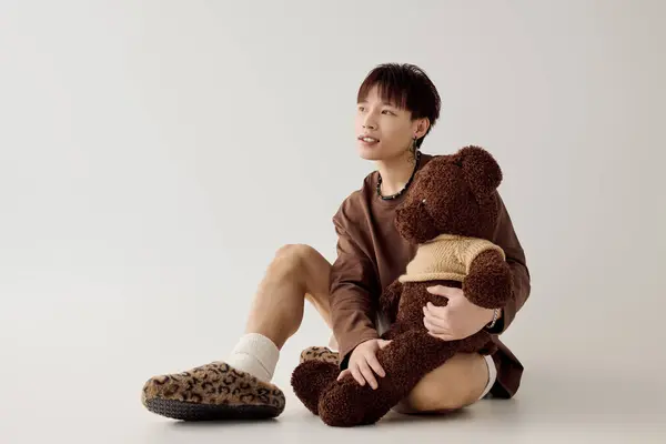 Le jeune homme s'assoit confortablement avec un ours en peluche, exsudant charme et chaleur dans un espace serein. — Photo de stock