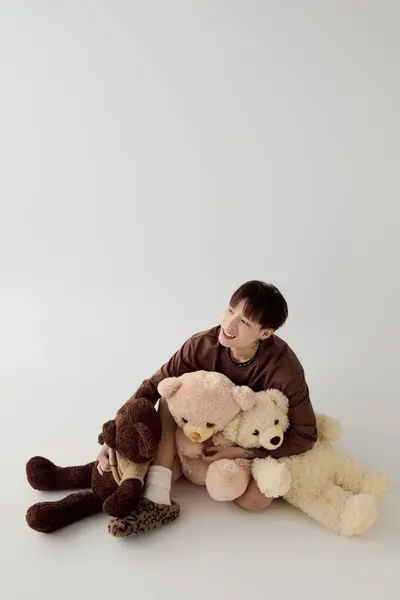 A young Asian man sits amidst plush teddy bears, expressing joy and warmth in a modern space. — Stock Photo