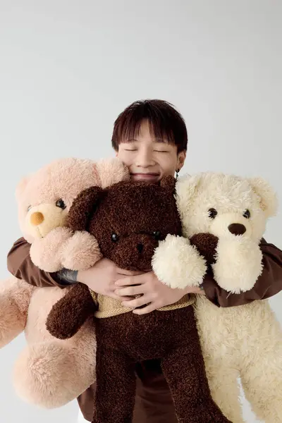 A smiling young man hugs three fluffy teddy bears in a warm, cheerful setting. — Stock Photo