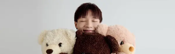 A young handsome Asian man smiles brightly while hugging three adorable teddy bears in a cozy room. — Stock Photo