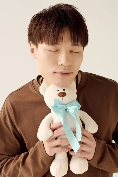Un jeune homme asiatique séduisant étreint doucement un ours en peluche, les yeux fermés dans une joie pure. — Photo de stock