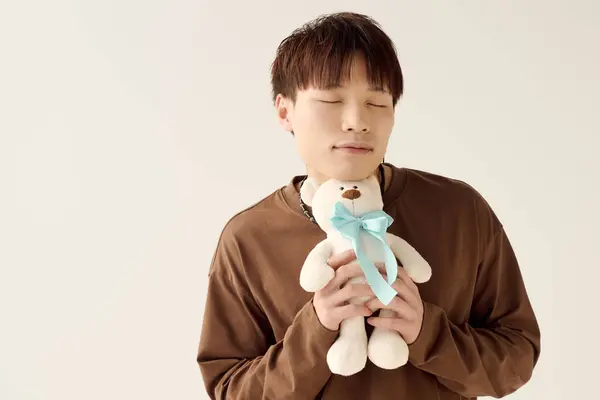 A young handsome asian man embraces a soft teddy bear with closed eyes, radiating warmth and joy. — Stock Photo