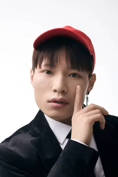 A young handsome asian man poses playfully, wearing a red cap, suit jacket, and expressing charm. — Stock Photo