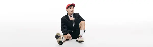 A young man showcases a relaxed demeanor, seated comfortably in a trendy outfit with a cap. — Stock Photo