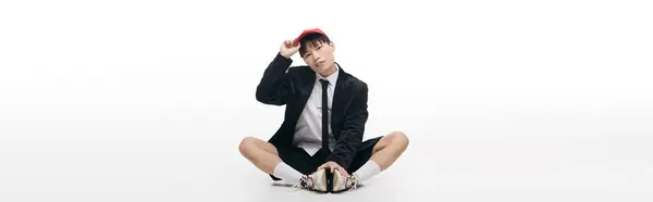 A young handsome Asian man in a suit and cap sits playfully on the floor. — Stock Photo