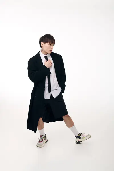 A handsome young Asian man showcases a modern fashion ensemble featuring shorts and a long coat. — Stock Photo
