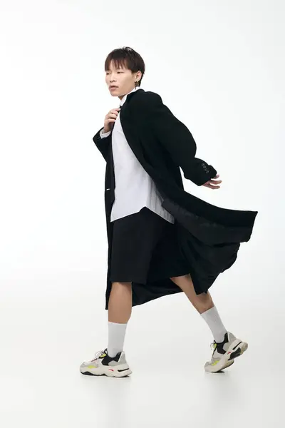 Confident young man dressed in a black coat and shorts strolls gracefully in a well lit space. — Stock Photo