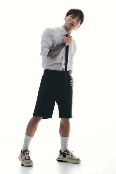 Dapper young asian man adjusting tie while showcasing modern fashion in a luminous environment — Stock Photo