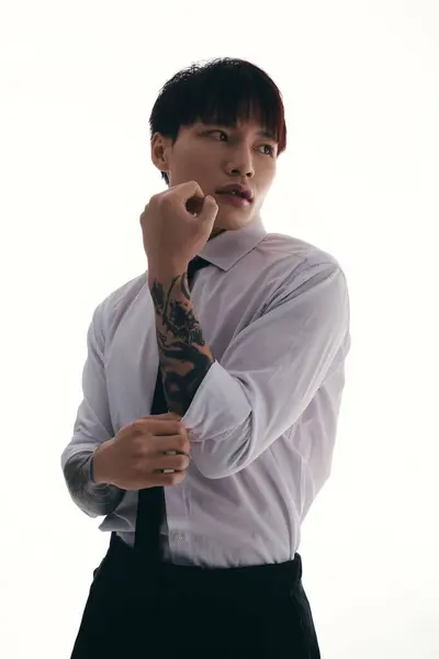 A young Asian man pulls up his shirt sleeve, revealing intricate tattoos under bright lights. — Stock Photo