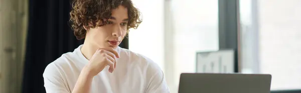 Attractive young man engages thoughtfully with his laptop in a bright office environment. — Stock Photo