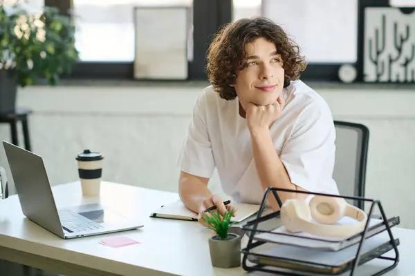 A thoughtful young man sits at his stylish office desk, surrounded by plants. — Stock Photo