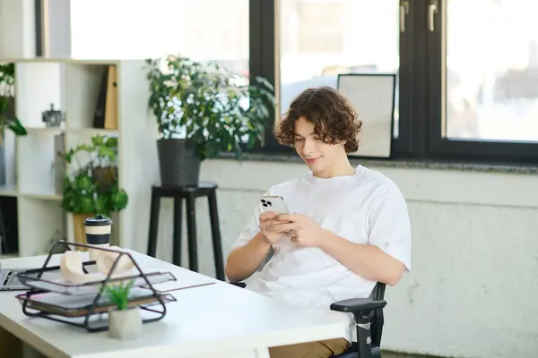 Handsome young man sits comfortably in an office chair, focused on his smartphone and smiling. — Stock Photo