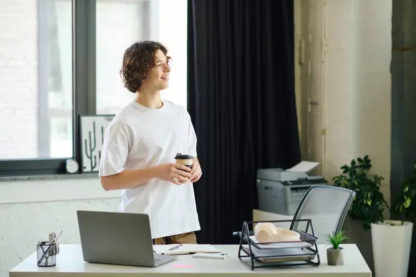 Un bel giovanotto si gode una pausa caffè nel suo ufficio contemplando i suoi compiti. — Foto stock