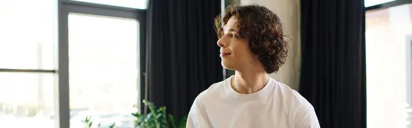 Young, attractive man with curly hair sits confidently in a vibrant office, contemplating his work. — Stock Photo
