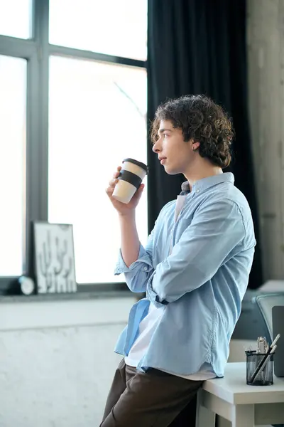 Bello giovane uomo si alza pensieroso in un ufficio elegante, sorseggiando caffè e osservando la vista. — Foto stock