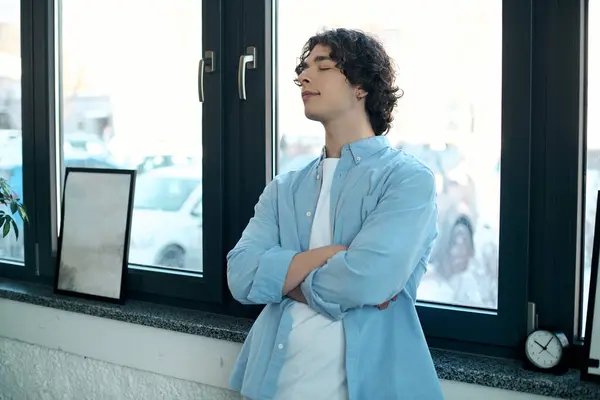 A young man stands confidently by a large office window, deep in thought. — Stock Photo