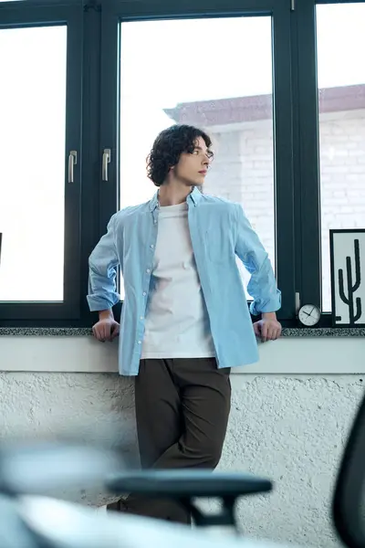 A young attractive man leans against a window in a contemporary office, contemplating his day. — Stock Photo