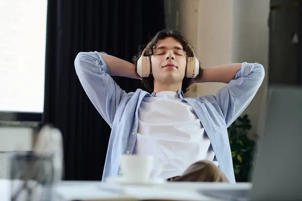 A handsome young man sits back in his office, headphones on, savoring a peaceful break from work. — Stock Photo
