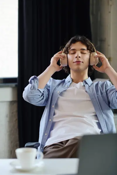 Man with curly hair wearing headphones relaxes at his desk, savoring a moment of calm and focus. — Stock Photo