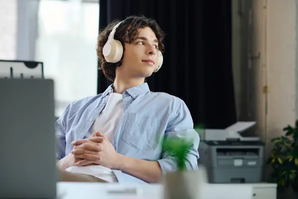 Handsome young man relaxes in a stylish office, wearing headphones and enjoying his day at work. — Stock Photo
