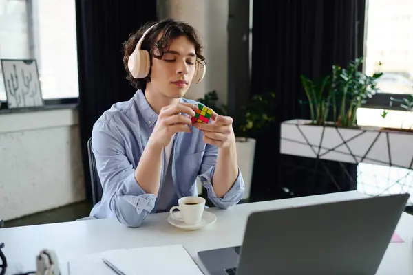 Focused young professional engages with a Rubiks cube while sipping coffee in a modern workspace. — Stock Photo