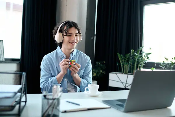 Escritório brilhante e moderno com um jovem focado resolvendo um cubo Rubiks enquanto ouve música. — Fotografia de Stock