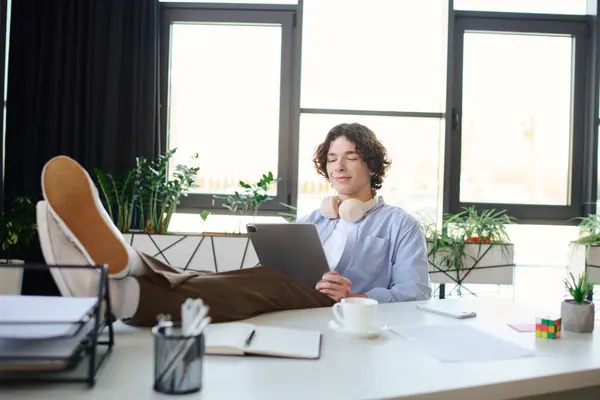 Young man sits comfortably in a stylish office space, engaging with his tablet and relaxing. — Stock Photo