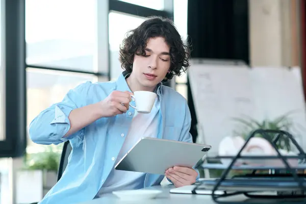 Handsome young professional sips coffee and focuses on work in bright, inviting office. — Stock Photo