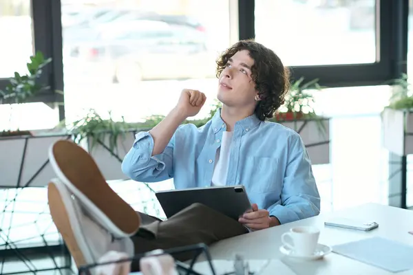 A young handsome man relaxes in an office, gazing thoughtfully while holding a tablet. — Stock Photo