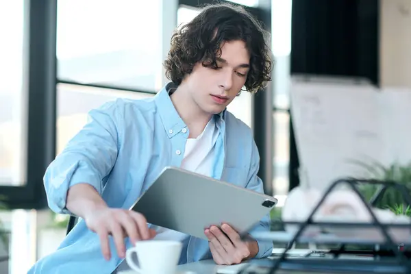 Handsome young man reviews information on a tablet while enjoying a cup of coffee in the office. — Stock Photo