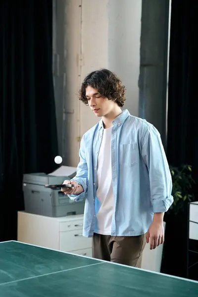 A young man stands in an office, focused, ready to skillfully hit a ping pong ball. — Stock Photo