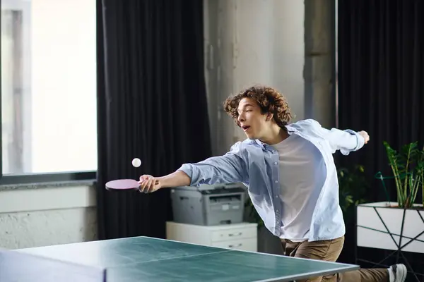 A young man happily plays table tennis in his stylish office, honing his skills. — Stock Photo