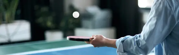 A handsome young man stands in a stylish office, ready to hit a ping pong ball with a paddle. — Stock Photo
