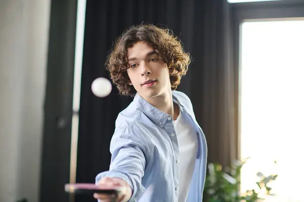 Young man with curly hair playfully tossing a ping pong ball while smiling in the office. — Stock Photo