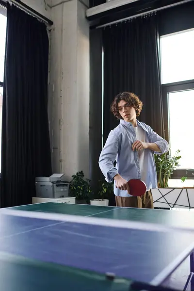 A young man plays table tennis in a modern office, surrounded by greenery. — Stock Photo