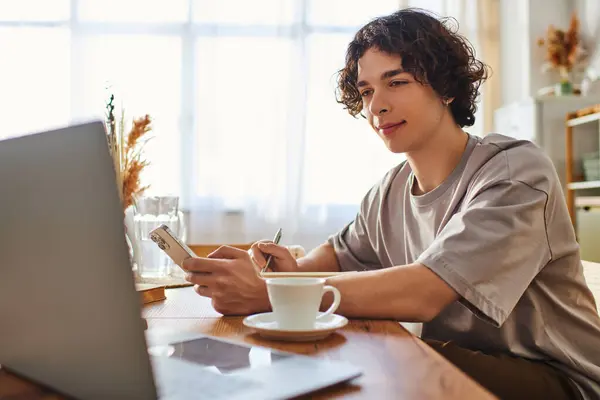 A young handsome man focuses on his smartphone in a cozy office, enjoying a cup of coffee. — Stock Photo