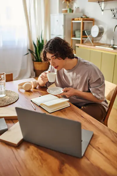 A young, attractive man sips coffee and takes notes at his desk in a bright and inviting office. — Stock Photo