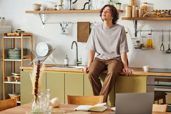 A young man relaxes on a counter in a modern office amid his work. — Stock Photo