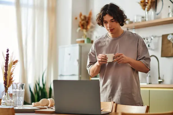 Engaging in work, a young man in casual attire holds a cup of coffee in a contemporary office. — Stock Photo