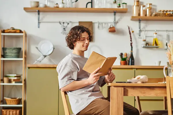 A young man sits at a wooden table, engrossed in a book amid stylish office decor. — Stock Photo